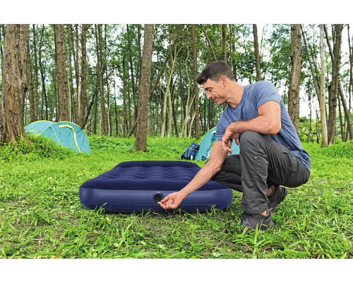 Mann bereitet eine Luftmatratze zum Campen vor dem Zelt vor.