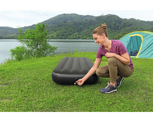 Frau pumpt eine Luftmatratze auf einem Campingplatz auf