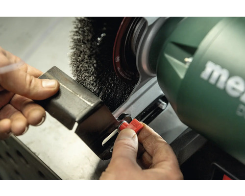 Eine Person verwendet eine Schleifbockmaschine mit Drahtbürste zum Entgraten eines Metallstücks. Metabo Logo.