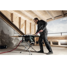 Ein Mann arbeitet mit einer Tischkreissäge in einem Raum mit Holzbalken an der Decke.