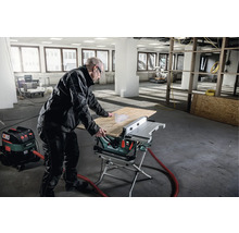 Mann arbeitet mit einer Tischkreissäge und einem Staubsauger in einem Raum.