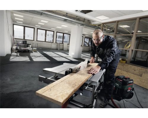 Handwerker sägt Holz mit einer Tischkreissäge in einem hellen Raum.