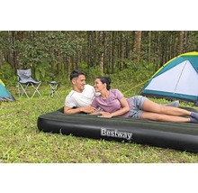Szene im Wald mit einem Paar, das auf einer Luftmatratze der Marke Bestway liegt, im Hintergrund Zelte und Campingstühle.