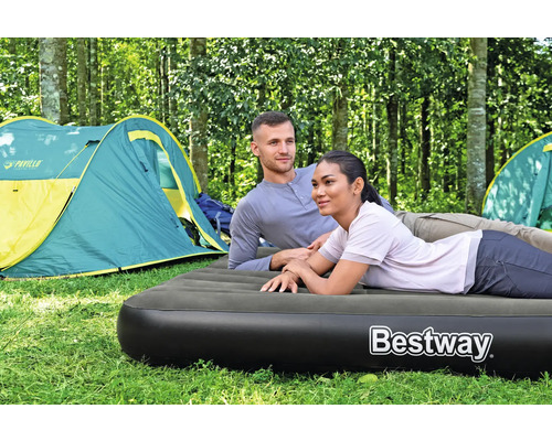 Ein Paar entspannt auf einer Luftmatratze beim Camping im Wald, Zelte im Hintergrund