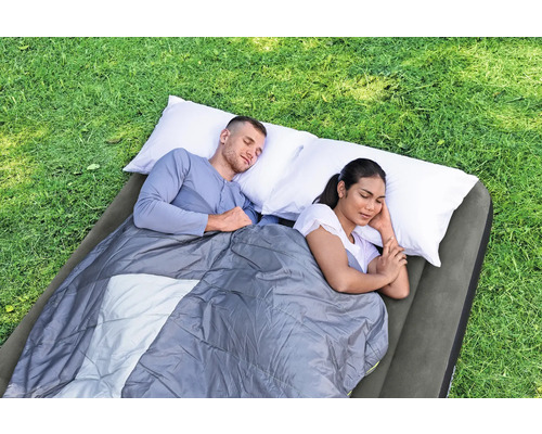 Zwei Personen schlafen auf einer Luftmatratze mit Schlafsack und Kissen im Freien.