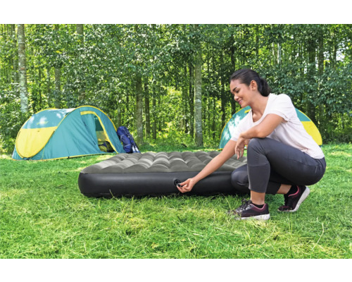 Frau bereitet eine Luftmatratze zum Campen vor einem Zelt vor.