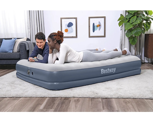 Zwei Personen entspannen auf einer grauen Bestway Luftmatratze im Wohnzimmer.