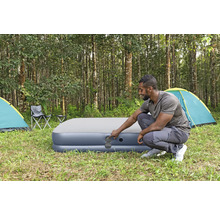 Mann bedient ein aufblasbares Gästebett auf einem Campingplatz mit Zelten und Stühlen.