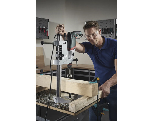 Ein Mann bohrt mit einer Tischbohrmaschine ein Loch in ein Holzbrett.