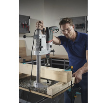 Mann bohrt mit einer Tischbohrmaschine ein Loch in ein Holzstück.