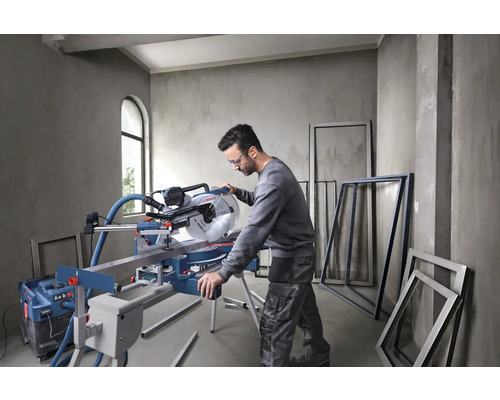 Mann arbeitet mit einer Kapp- und Gehrungssäge in einem Raum mit Fensterrahmen.