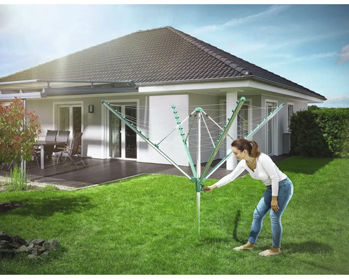 Frau bedient Wäschespinne im Garten vor dem Haus