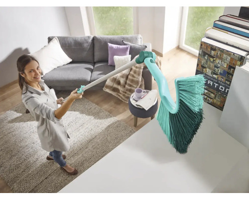 Frau benutzt eine Bürste mit Stiel zur Reinigung im Wohnzimmer.