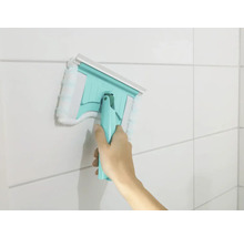 Hand die einen Fensterwischer mit Mikrofaserbezug an einer gefliesten Wand verwendet