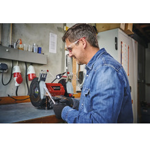 Mann schleift Metall an einem Einhell Doppelschleifer in einer Werkstatt.