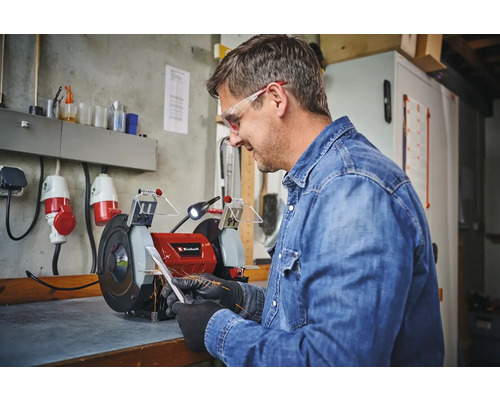 Mann schleift Metall an einem Einhell Doppelschleifer in einer Werkstatt.