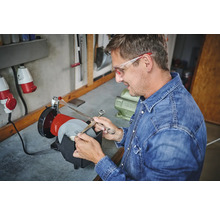 Mann schärft Schere mit Schleifmaschine in Werkstatt