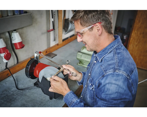 Mann schärft Schere mit Schleifmaschine in Werkstatt