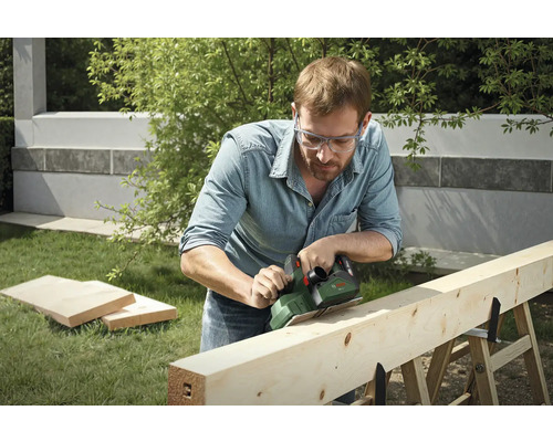 Mann hobelt Holzbalken im Garten mit Elektrohobel der Marke Bosch