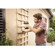 Mann befestigt Holzspalier mit Akkuschrauber an Hauswand