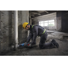 Ein Bauarbeiter kniet in einem Rohbau und sägt ein Rohr mit einer Säbelsäge.