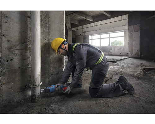 Ein Bauarbeiter kniet in einem Rohbau und sägt ein Rohr mit einer Säbelsäge.