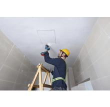 Handwerker schneidet mit einer Säbelsäge eine Deckenöffnung von einer Leiter aus.