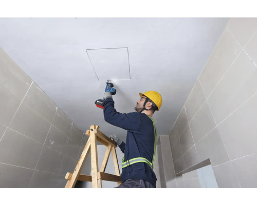 Handwerker schneidet mit einer Säbelsäge eine Deckenöffnung von einer Leiter aus.