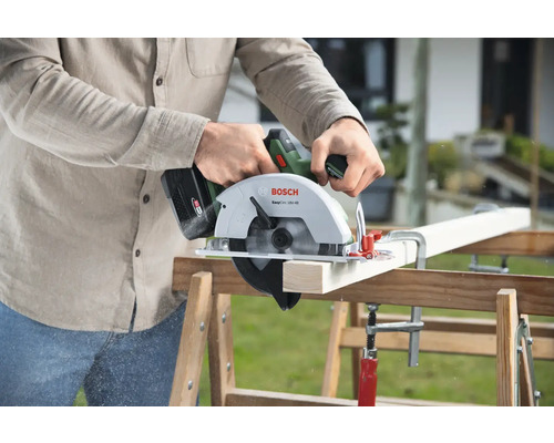 Eine Person sägt ein Holzbrett mit einer Bosch Akku-Handkreissäge auf einer Werkbank.