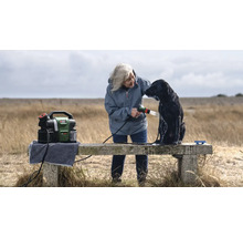 Frau wäscht Hund mit einem tragbaren Hochdruckreiniger von Bosch im Freien.