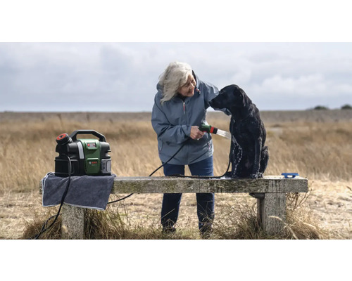 Frau wäscht Hund mit einem tragbaren Hochdruckreiniger von Bosch im Freien.