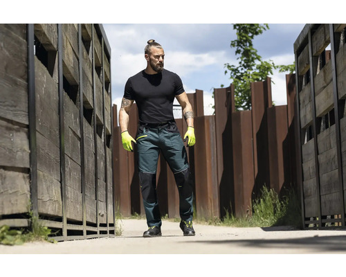 Mann trägt Arbeitshose mit Knieverstärkung, Arbeitshandschuhe und T-Shirt im Freien