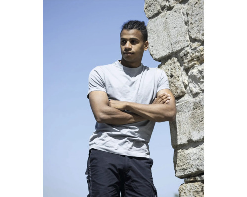 Mann in grauem T-Shirt und Cargo-Shorts, der an einer Steinmauer lehnt