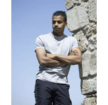 Mann mit verschränkten Armen, angelehnt an eine Steinmauer, trägt ein T-Shirt und Shorts