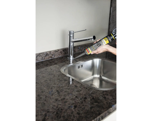 Auftragen von Dichtmasse um eine Spüle mit Armatur auf einer Arbeitsplatte