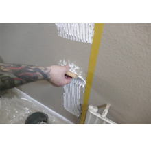 Eine Person trägt Fliesenkleber mit einer Spachtel auf eine Wand auf.