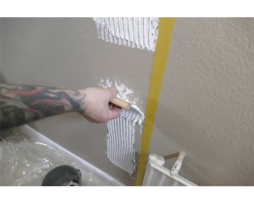 Eine Person trägt Fliesenkleber mit einer Spachtel auf eine Wand auf.
