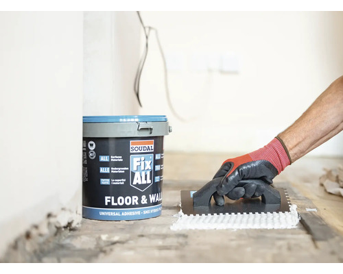 Ein Eimer Soudal Fix ALL Klebstoff und eine Person, die Klebstoff mit einer Kelle aufträgt.