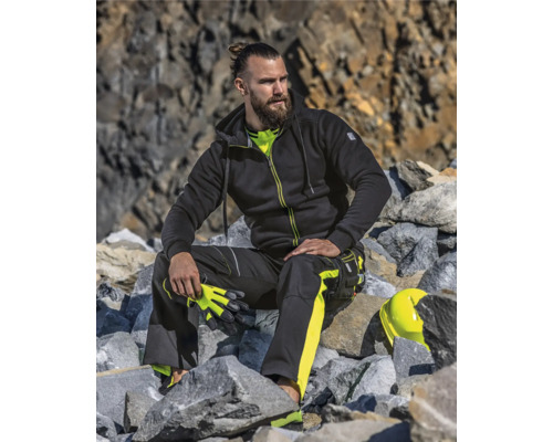 Mann in Arbeitskleidung mit Kapuzenjacke und Arbeitshose sitzt auf Steinen.