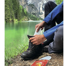 Person legt eine Schuhsohle in einen Wanderschuh vor einer Berglandschaft