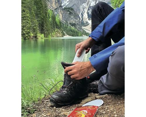 Person legt eine Schuhsohle in einen Wanderschuh vor einer Berglandschaft