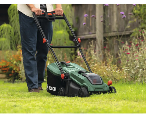 Eine Person bedient einen grünen Rasenmäher von Bosch auf einem Rasen.