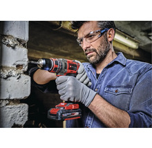 Mann bohrt mit einer Einhell Akku-Bohrmaschine in eine Ziegelwand. Er trägt Schutzbrille und Handschuhe.