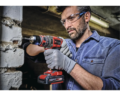 Mann bohrt mit einer Einhell Akku-Bohrmaschine in eine Ziegelwand. Er trägt Schutzbrille und Handschuhe.