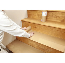 Eine Person deckt eine Holztreppe mit Schutzpapier ab.