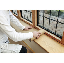 Eine Person rollt Schutzpapier auf einer Fensterbank aus Holz aus.