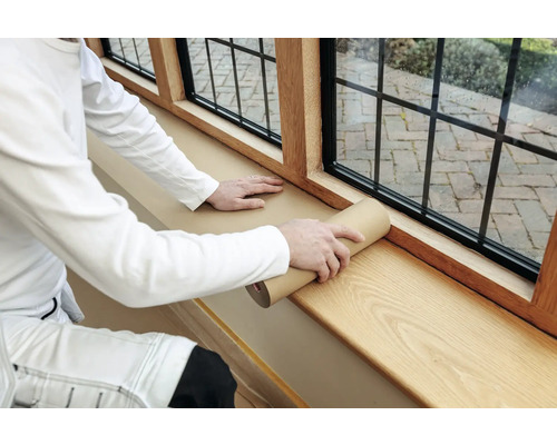 Eine Person rollt Schutzpapier auf einer Fensterbank aus Holz aus.