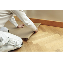 Handwerker rollt Abdeckpapier auf einem Holzboden aus