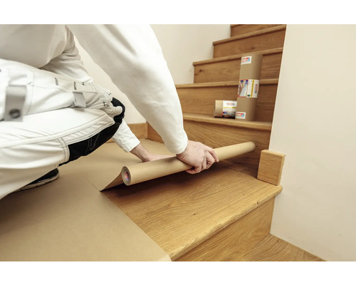 Eine Person bedeckt eine Holztreppe mit Abdeckpapier.