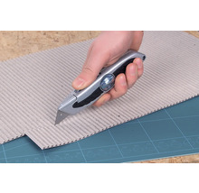 Eine Hand schneidet mit einem Universalmesser Pappe.